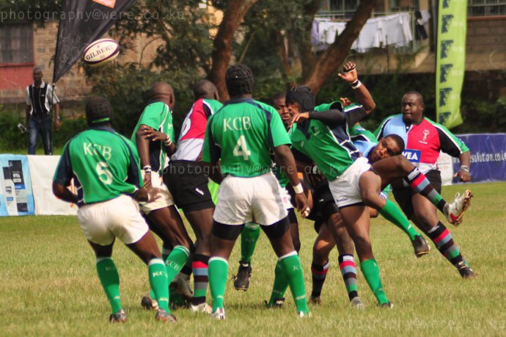 Players from KCB and Quins engaged in a rugby match, with a player kicking the ball.